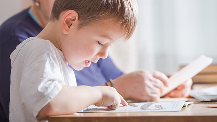 Four-year-old boy sounding out words while reading with his teacher